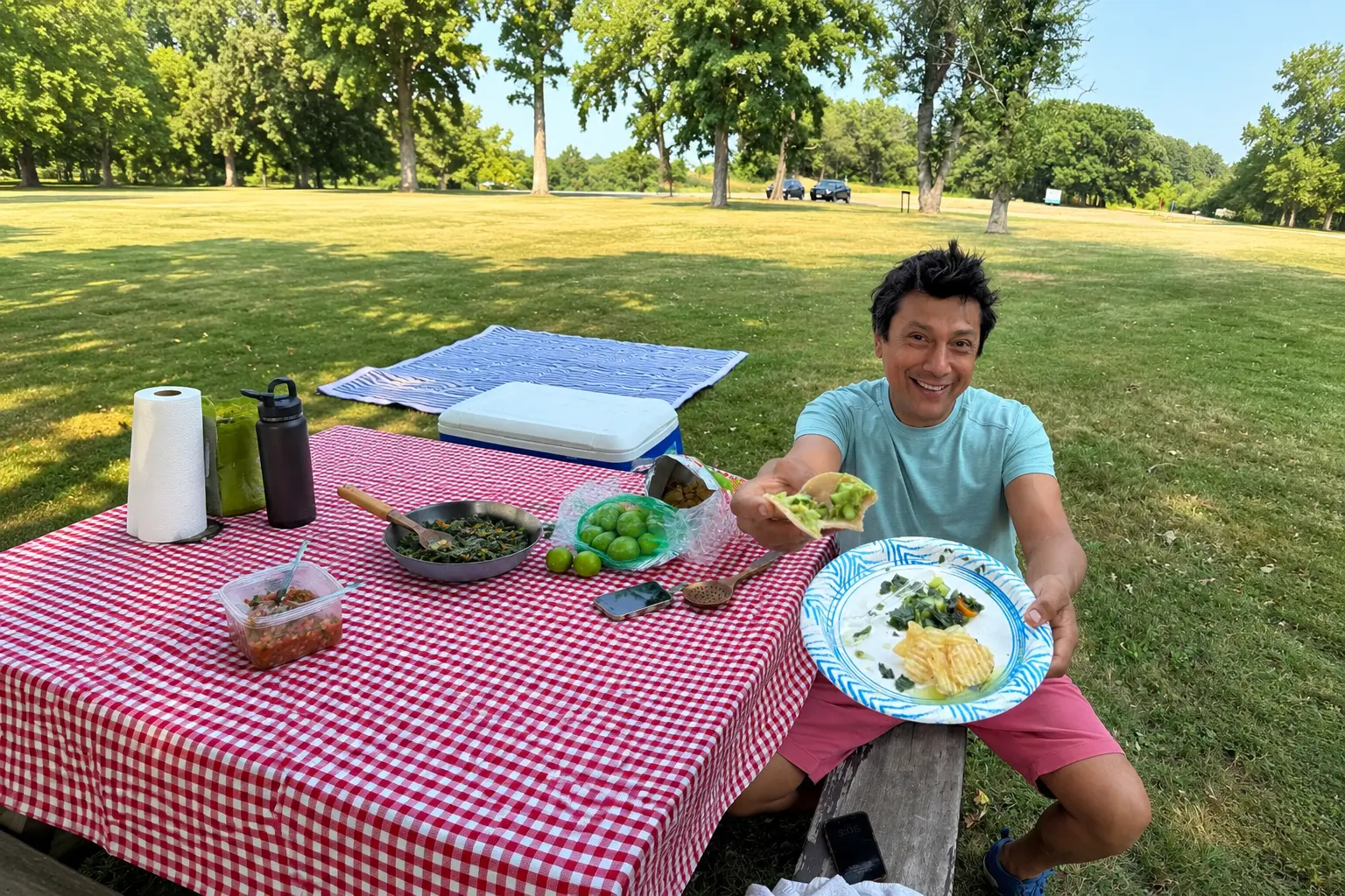 Jose smiling at a park picnic table holding a plant-based taco and a plate of greens